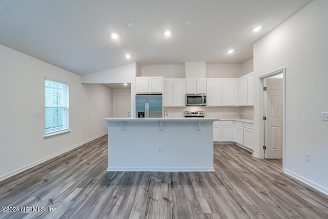 kitchen featuring white cabinetry, light hardwood / wood-style floors, a center island with sink, appliances with stainless steel finishes, and a breakfast bar