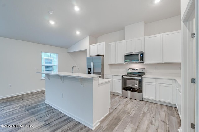 kitchen featuring light wood-type flooring, stainless steel appliances, white cabinets, and an island with sink