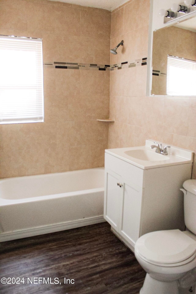 full bathroom with tiled shower / bath, wood-type flooring, tile walls, vanity, and toilet