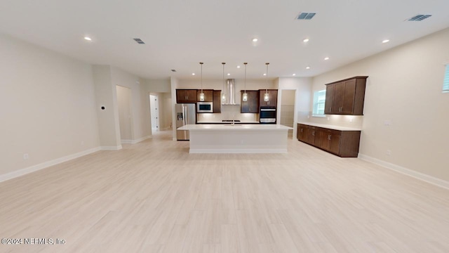 kitchen with dark brown cabinetry, hanging light fixtures, light hardwood / wood-style flooring, a kitchen island with sink, and appliances with stainless steel finishes