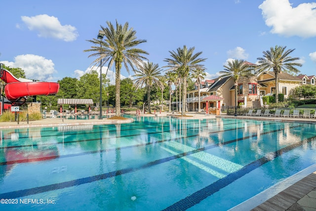 community pool with a water slide, a patio area, and fence