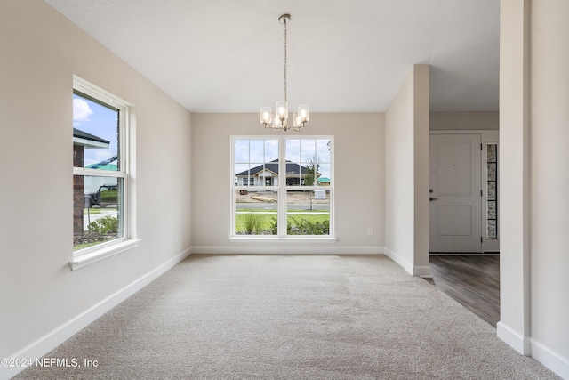 unfurnished dining area featuring plenty of natural light, baseboards, a notable chandelier, and carpet flooring