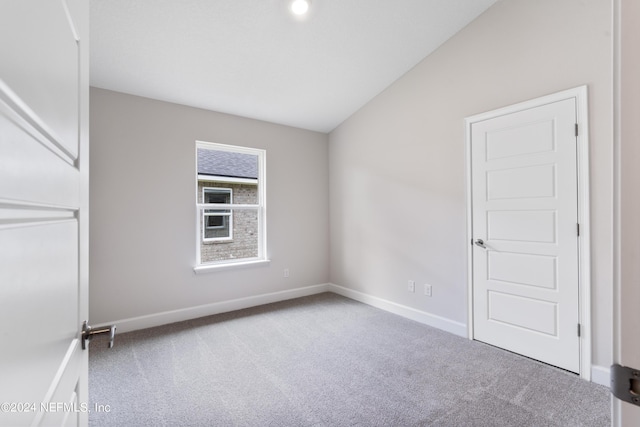 carpeted empty room featuring baseboards and vaulted ceiling