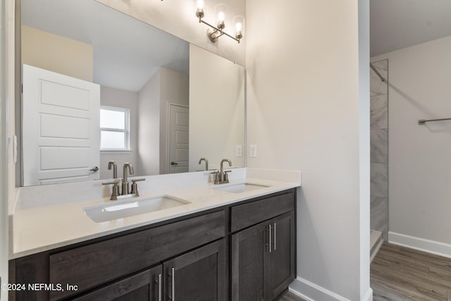 full bath featuring a tile shower, double vanity, a sink, and baseboards