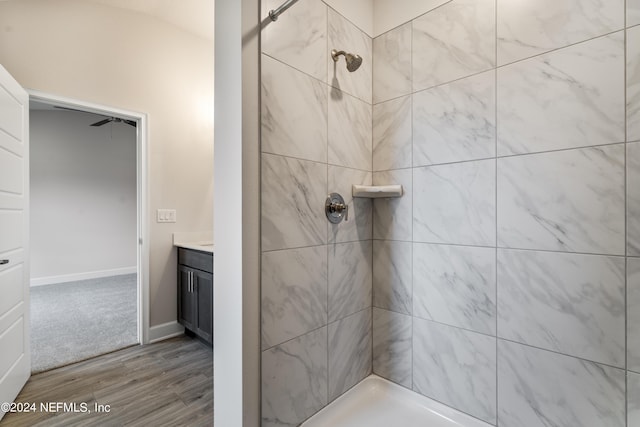 bathroom with baseboards, wood finished floors, tiled shower, and vanity