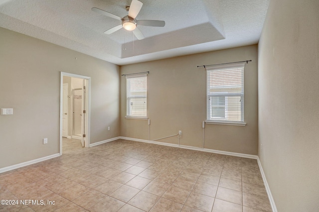 unfurnished room with a raised ceiling, ceiling fan, light tile floors, and a textured ceiling