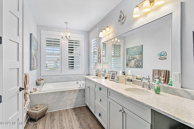 bathroom with large vanity, a relaxing tiled bath, hardwood / wood-style flooring, a notable chandelier, and dual sinks