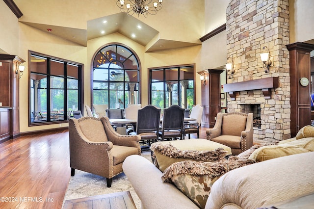 living room featuring a stone fireplace, decorative columns, a high ceiling, dark wood-type flooring, and an inviting chandelier