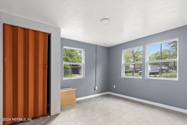 interior space with a textured ceiling, a closet, light tile floors, and multiple windows