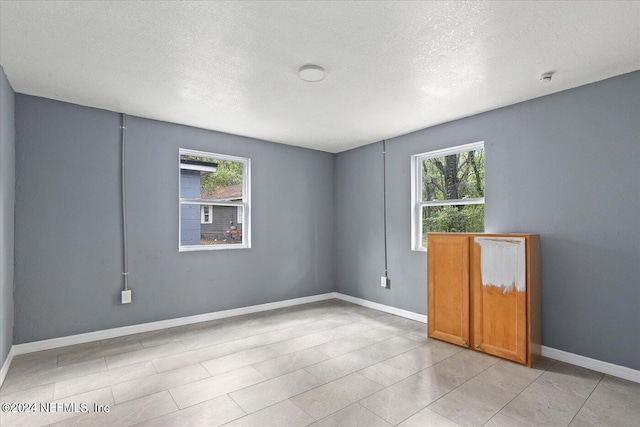 empty room with a textured ceiling, a wealth of natural light, and light tile floors