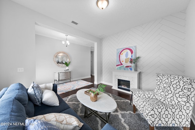 living room featuring wood-type flooring, a premium fireplace, a textured ceiling, and an inviting chandelier