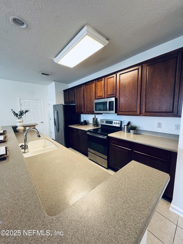 kitchen with a textured ceiling, stainless steel appliances, a sink, visible vents, and light countertops