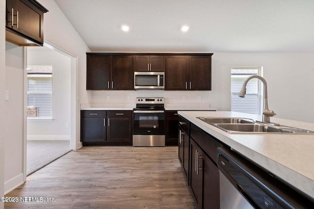 kitchen featuring dark brown cabinetry, appliances with stainless steel finishes, light countertops, light wood-type flooring, and a sink