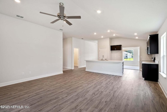 unfurnished living room with baseboards, visible vents, dark wood-type flooring, vaulted ceiling, and a sink