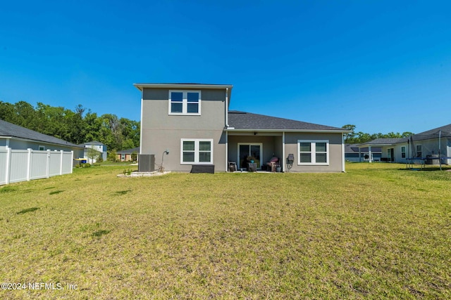 rear view of house with a trampoline, a yard, central AC unit, and a patio