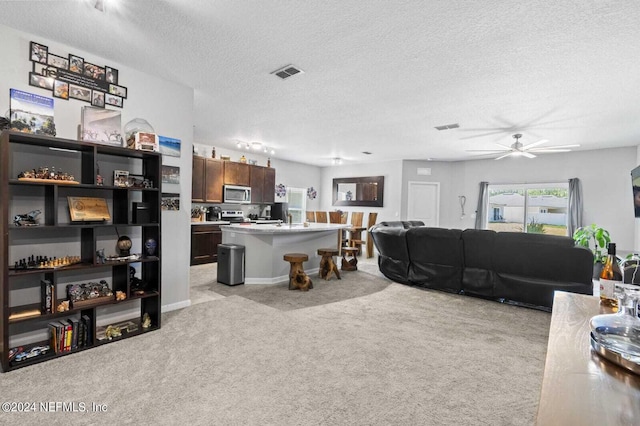 living room with light carpet, ceiling fan, and a textured ceiling