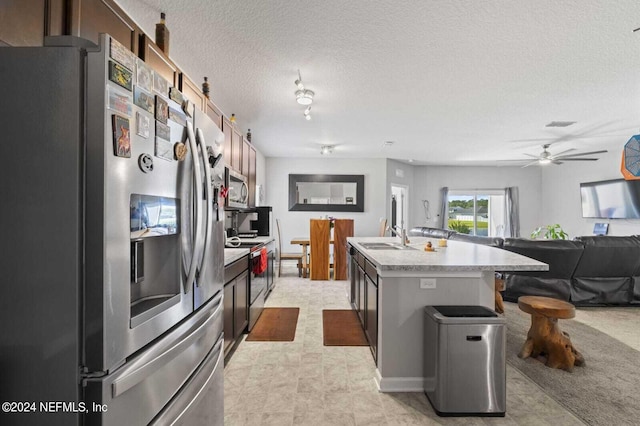 kitchen with ceiling fan, a textured ceiling, a kitchen bar, stainless steel appliances, and a center island with sink