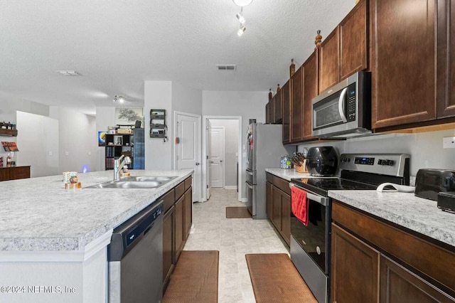 kitchen with stainless steel appliances, track lighting, a textured ceiling, sink, and light tile floors