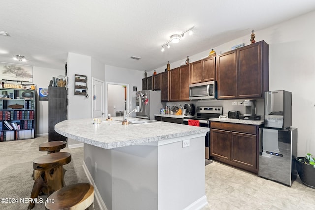 kitchen featuring dark brown cabinets, appliances with stainless steel finishes, an island with sink, and rail lighting