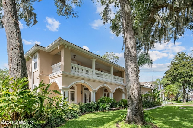 back of house with a lawn and a balcony