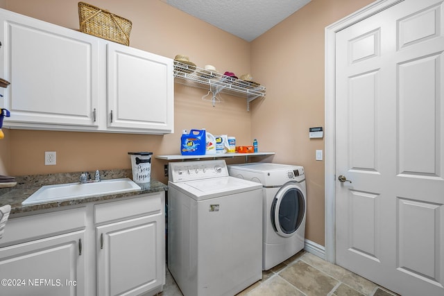 laundry room featuring a textured ceiling, cabinets, sink, and washing machine and clothes dryer