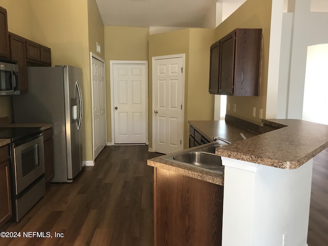 kitchen featuring dark wood-style flooring, stainless steel appliances, a sink, dark brown cabinetry, and a peninsula