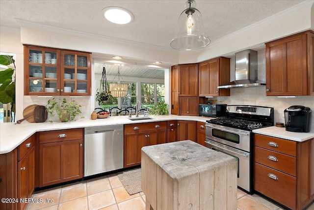 kitchen featuring sink, decorative light fixtures, a textured ceiling, appliances with stainless steel finishes, and wall chimney range hood