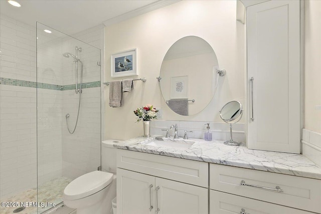 bathroom with vanity, crown molding, toilet, and a tile shower