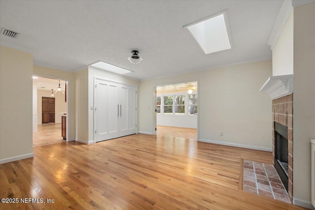 unfurnished living room featuring ornamental molding, light wood-type flooring, a fireplace, and a skylight