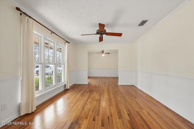 unfurnished room featuring visible vents, a wainscoted wall, ornamental molding, wood finished floors, and a textured ceiling