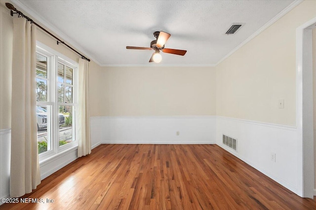 empty room featuring a textured ceiling, visible vents, wood finished floors, and ornamental molding