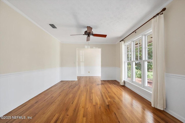 empty room with ornamental molding, ceiling fan, a textured ceiling, and light wood-type flooring