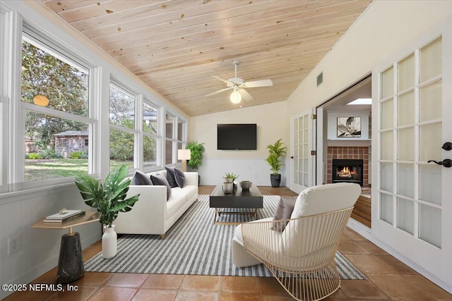 sunroom featuring vaulted ceiling, wooden ceiling, a tile fireplace, and french doors