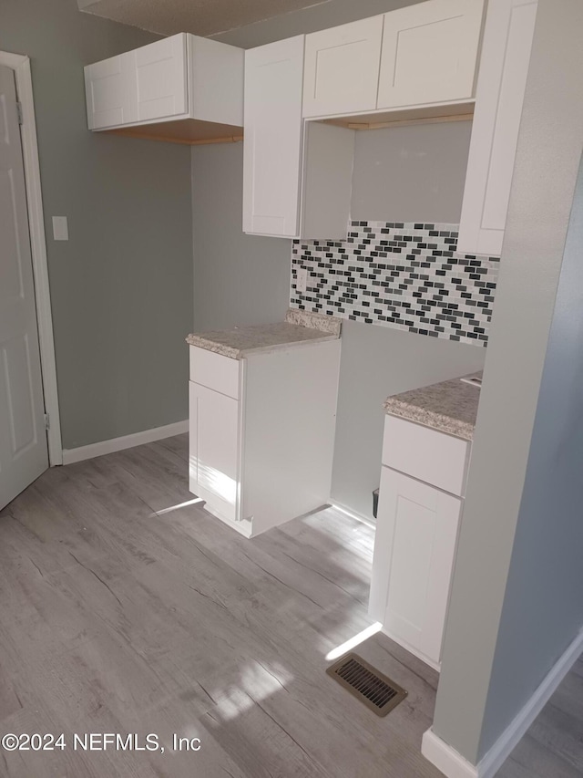 kitchen featuring tasteful backsplash, light wood-type flooring, and white cabinetry