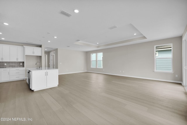 kitchen with white cabinetry, light hardwood / wood-style flooring, a center island with sink, and a tray ceiling