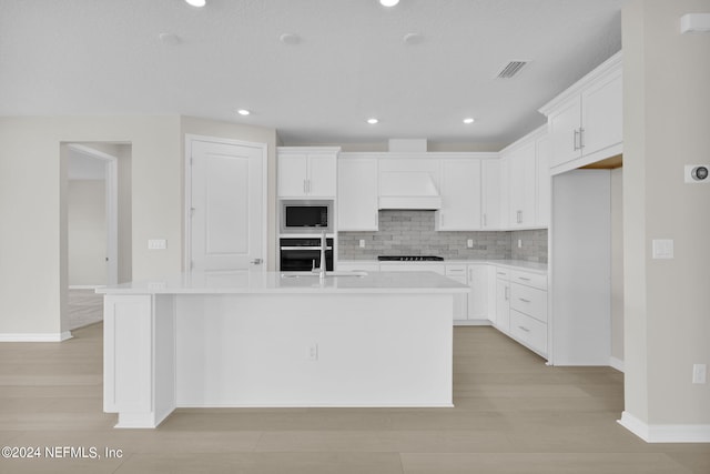 kitchen with white cabinetry, sink, appliances with stainless steel finishes, tasteful backsplash, and a kitchen island with sink