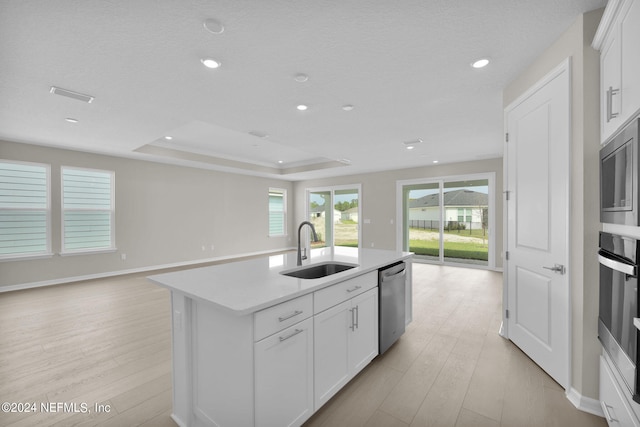 kitchen with a kitchen island with sink, appliances with stainless steel finishes, sink, white cabinets, and light hardwood / wood-style flooring