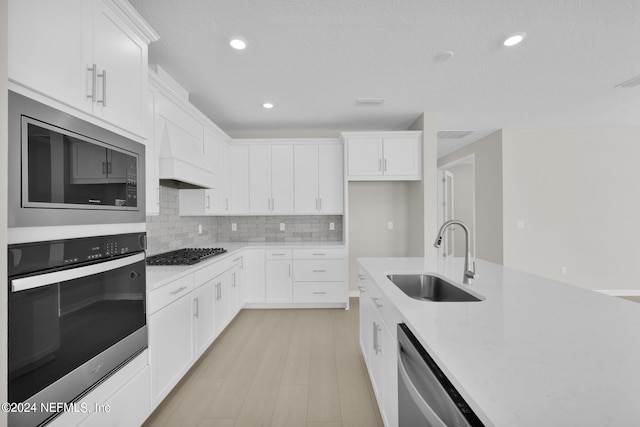 kitchen featuring stainless steel appliances, white cabinets, decorative backsplash, sink, and light hardwood / wood-style flooring