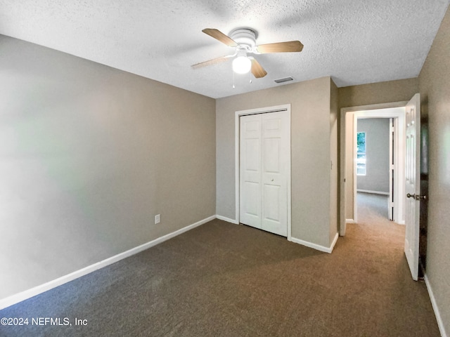 unfurnished bedroom featuring dark colored carpet, a closet, ceiling fan, and a textured ceiling