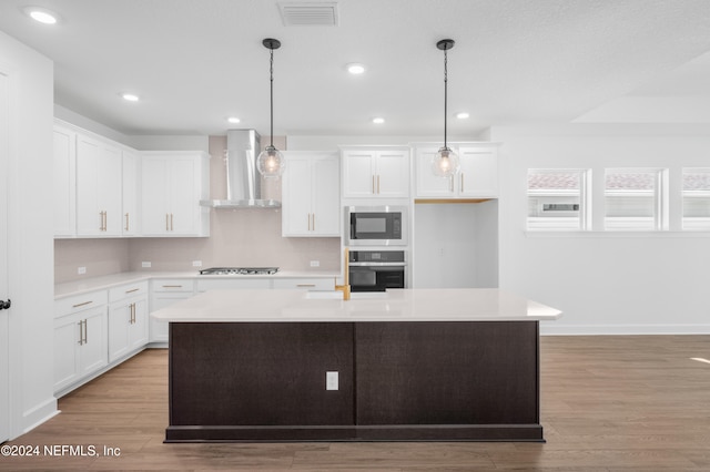 kitchen with stainless steel appliances, wall chimney range hood, a center island with sink, and white cabinets