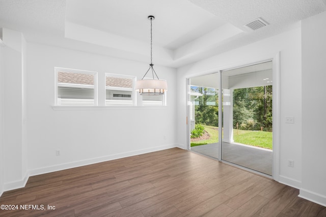 unfurnished dining area featuring dark wood-type flooring, a textured ceiling, and a raised ceiling