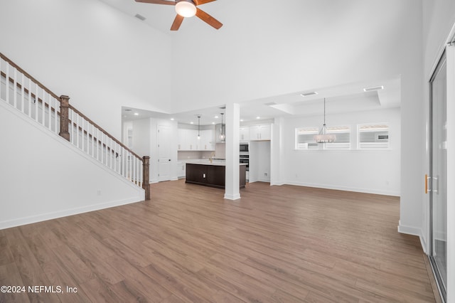 unfurnished living room with a towering ceiling, hardwood / wood-style floors, and ceiling fan