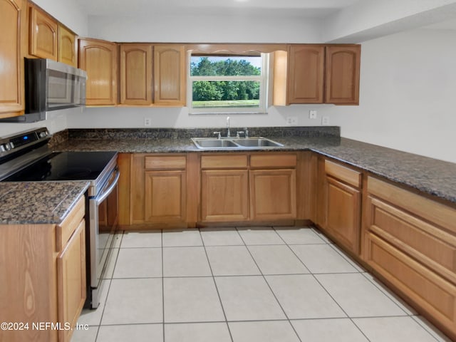 kitchen featuring dark stone countertops, sink, stainless steel appliances, and light tile floors