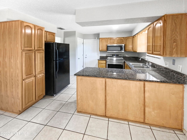 kitchen featuring light tile flooring, kitchen peninsula, appliances with stainless steel finishes, sink, and dark stone countertops