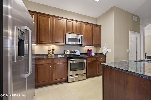 kitchen with appliances with stainless steel finishes, light tile patterned floors, dark stone counters, and decorative columns