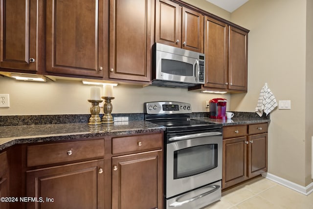 kitchen with dark stone countertops, stainless steel appliances, and light tile patterned floors