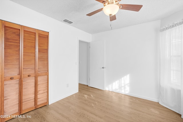 unfurnished bedroom with light hardwood / wood-style floors, a closet, a textured ceiling, and ceiling fan