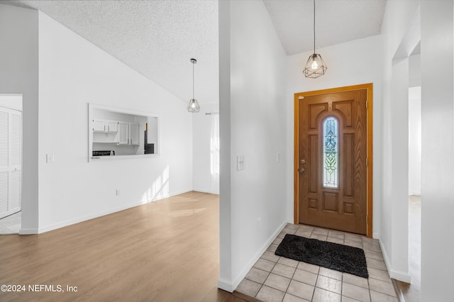 entrance foyer with a textured ceiling, high vaulted ceiling, and light wood-type flooring