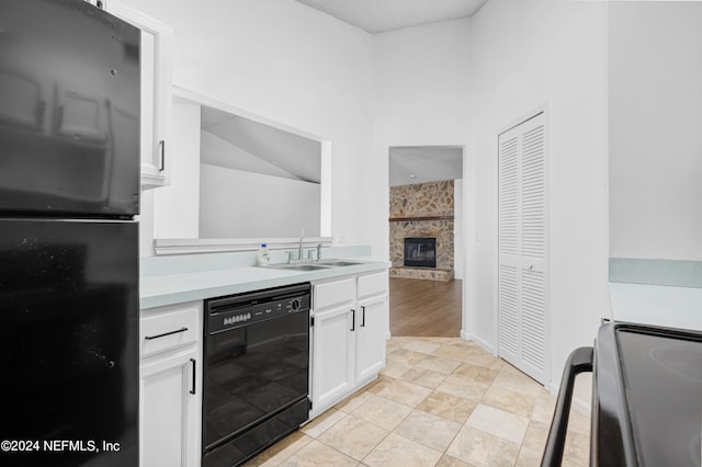 kitchen with lofted ceiling, a stone fireplace, sink, black appliances, and white cabinetry