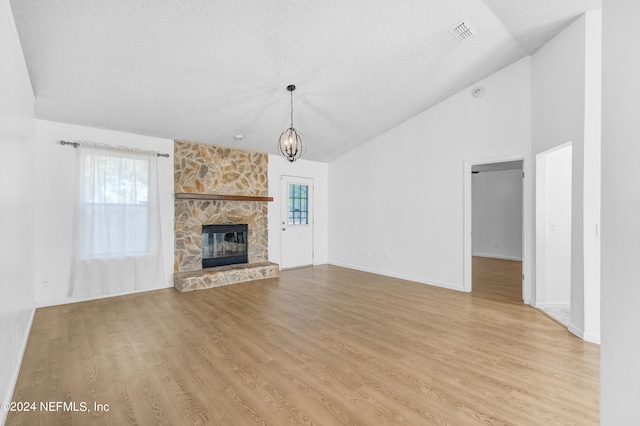 unfurnished living room with a stone fireplace, a textured ceiling, light hardwood / wood-style floors, high vaulted ceiling, and a chandelier